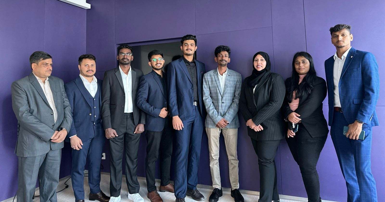 Nine Missan staff in business suits standing in a row against a purple wall