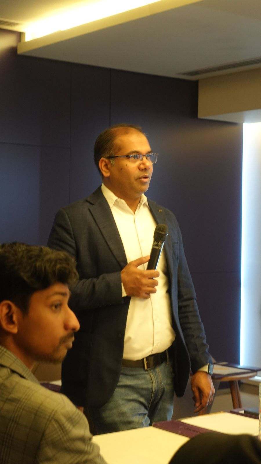 A Missan team member speaking into a microphone, with a colleague listening in the foreground