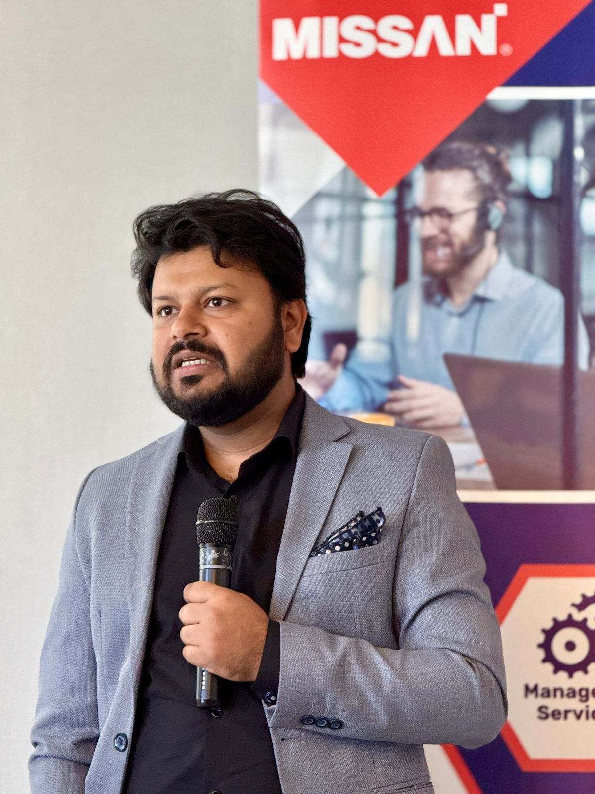 A Missan team member speaking into a microphone under a large Missan banner