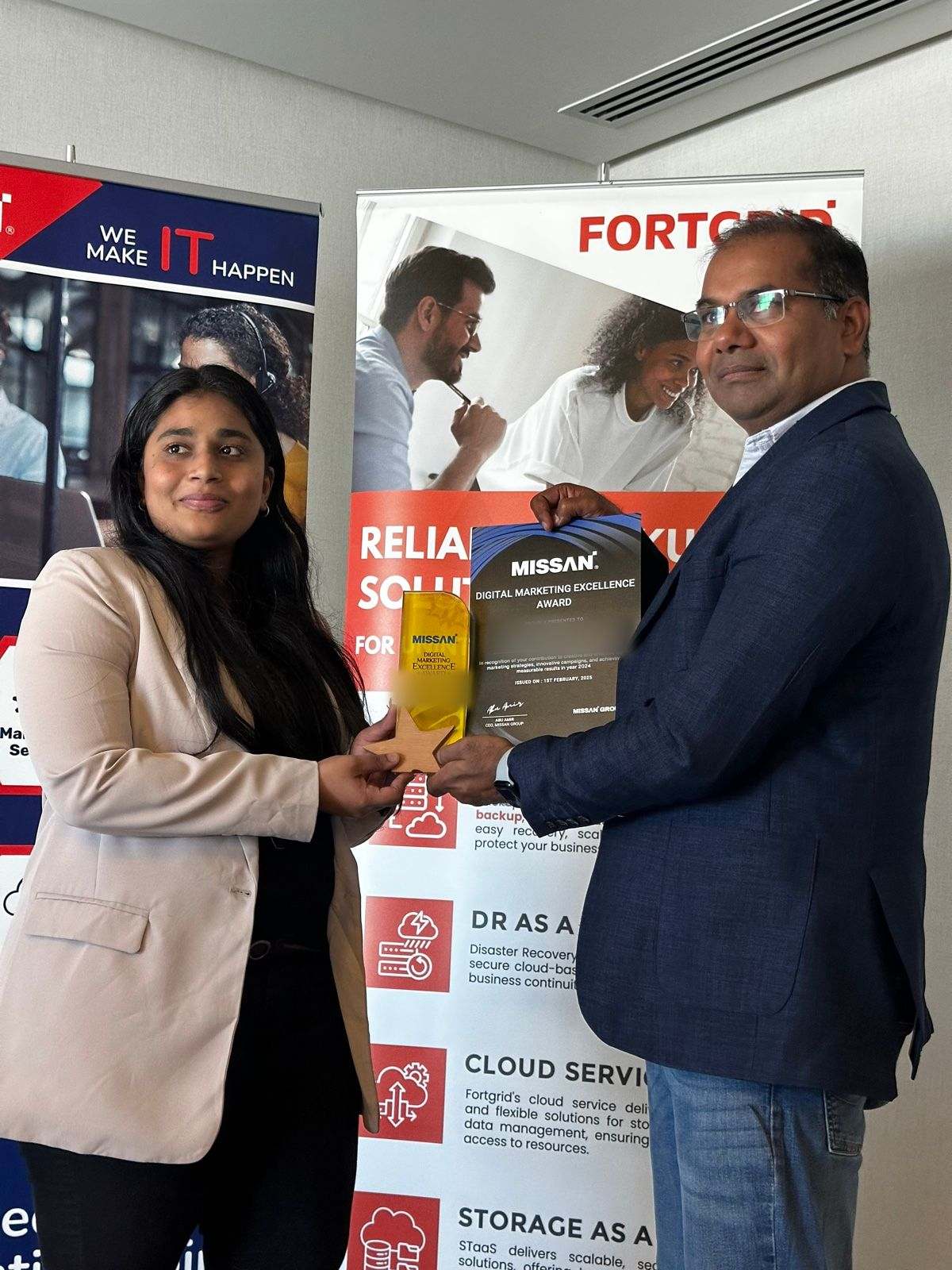 A Missan team member presenting a colleague with a trophy and certificate in front of a FortGrid banner