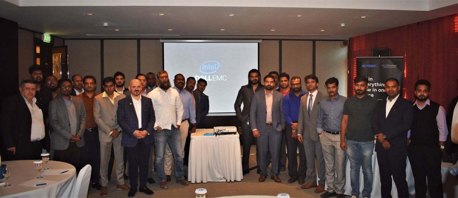 About thirty people in a wide group photo in a hotel function room, under a screen showing the Intel and Dell EMC logos