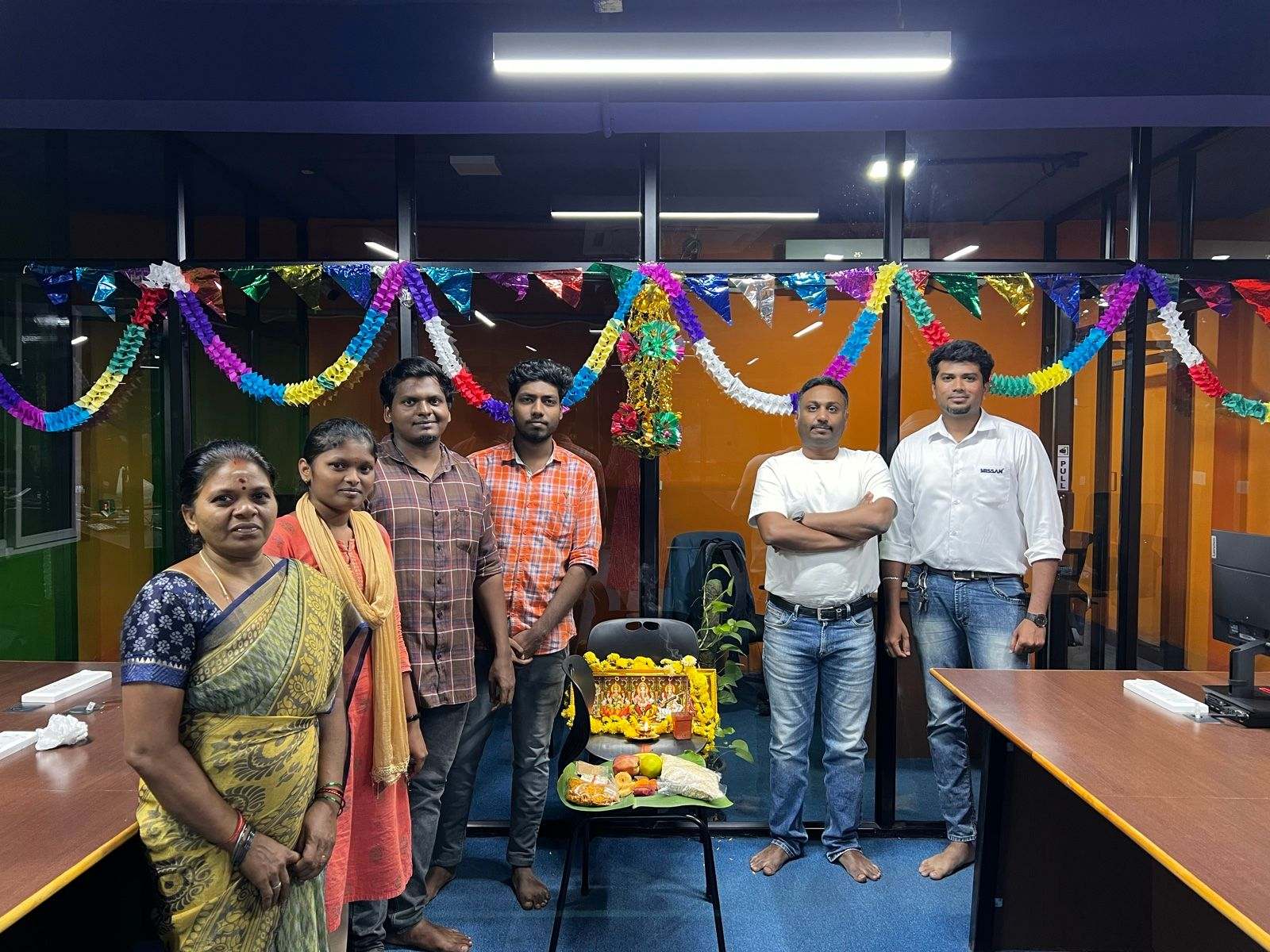 Seven members of Missan's India team standing beside a decorated pooja set-up under festive garlands