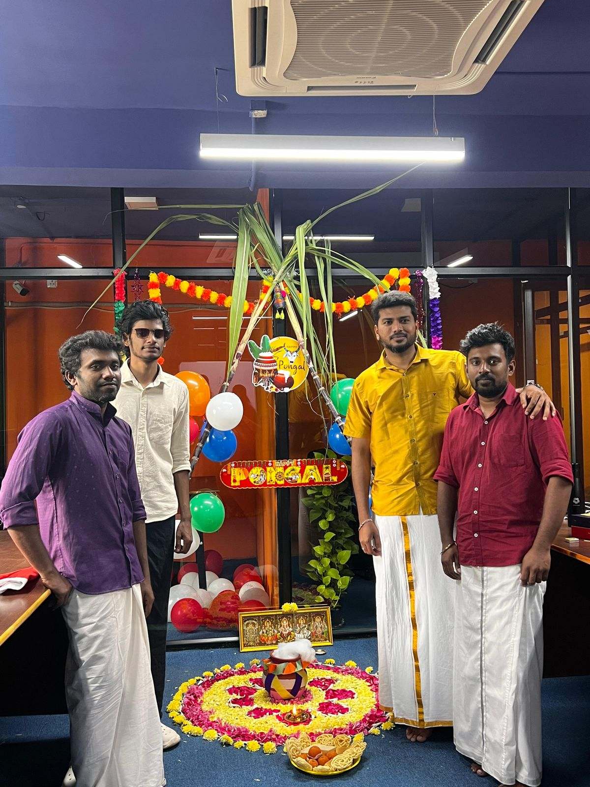 Four men from Missan's India team in veshti beside Pongal decorations