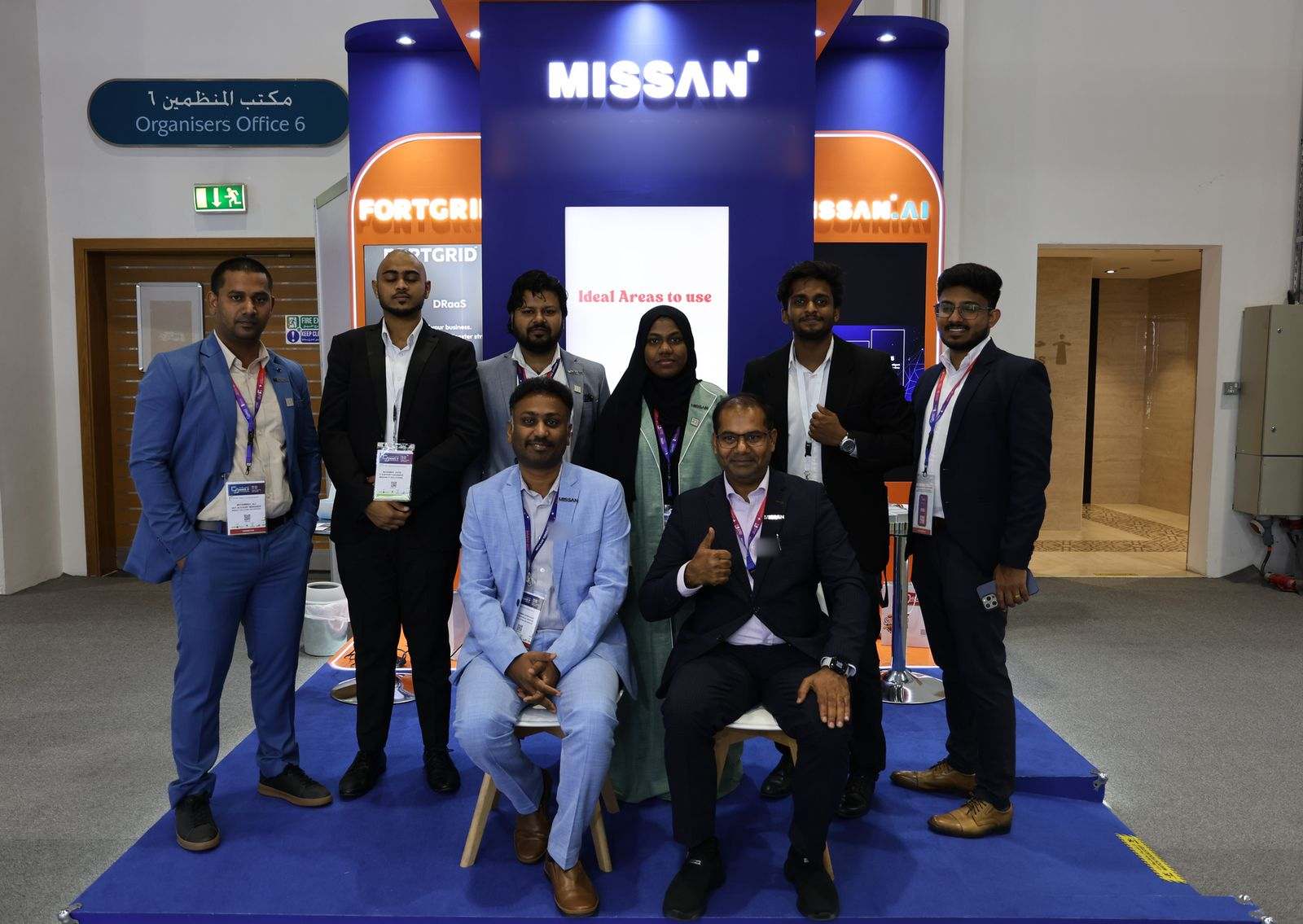 Eight Missan team members, two seated and six standing, on the Missan stand under the MISSAN sign, with FortGrid and Missan.AI panels either side