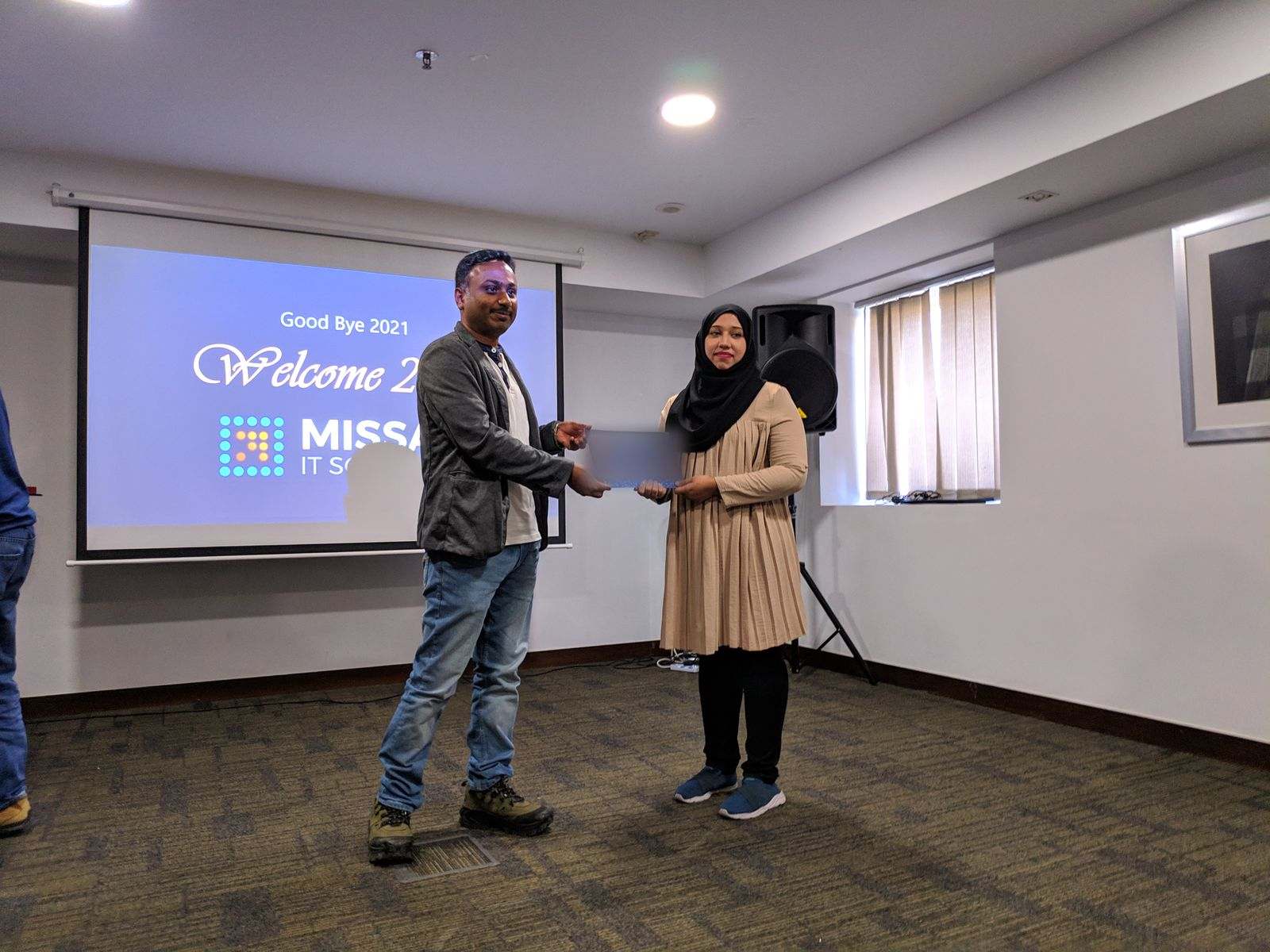 Two Missan staff on stage with a certificate in front of a screen reading Good Bye 2021, Welcome 2022