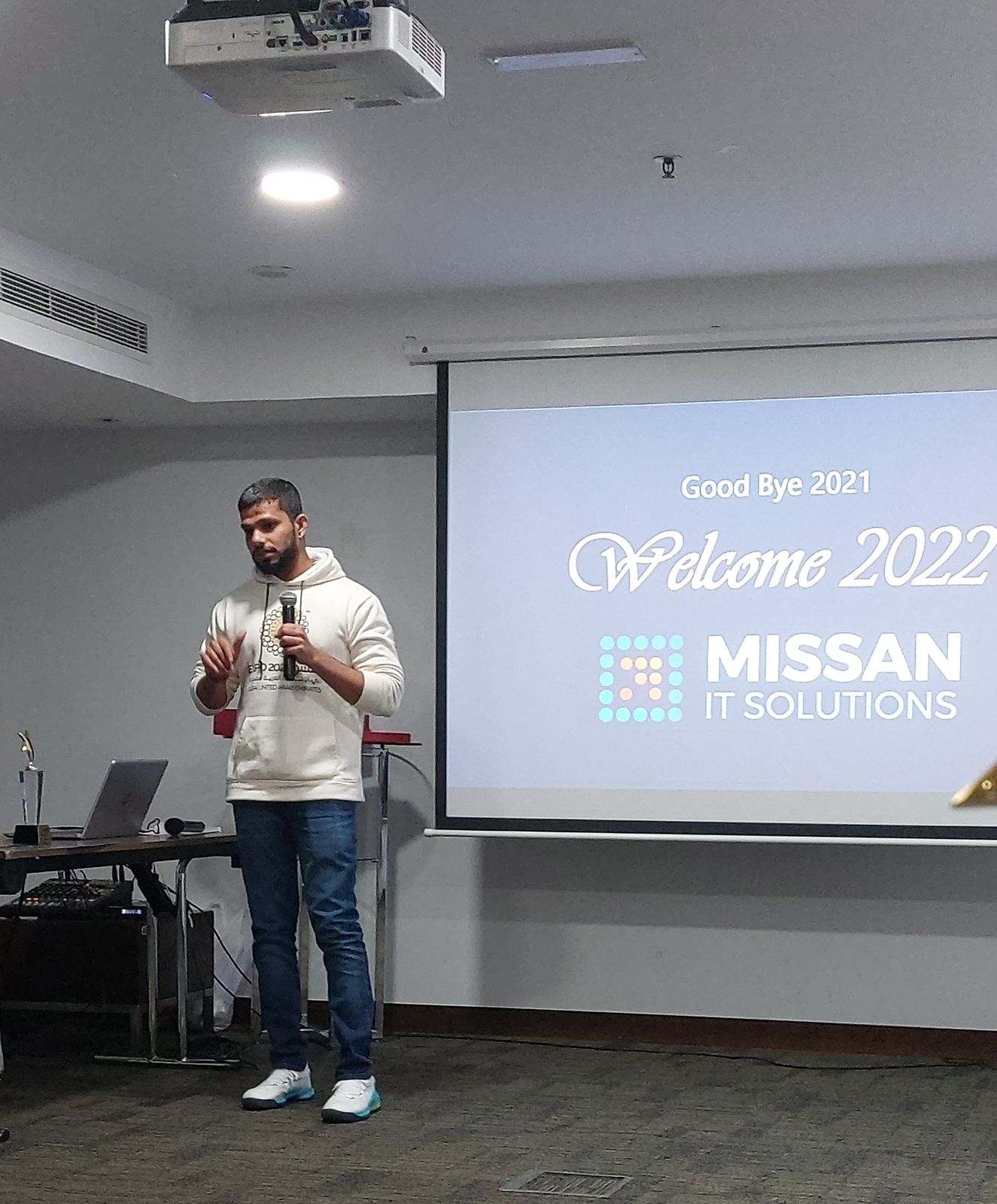 A Missan team member speaking into a microphone beside a large Welcome 2022 screen