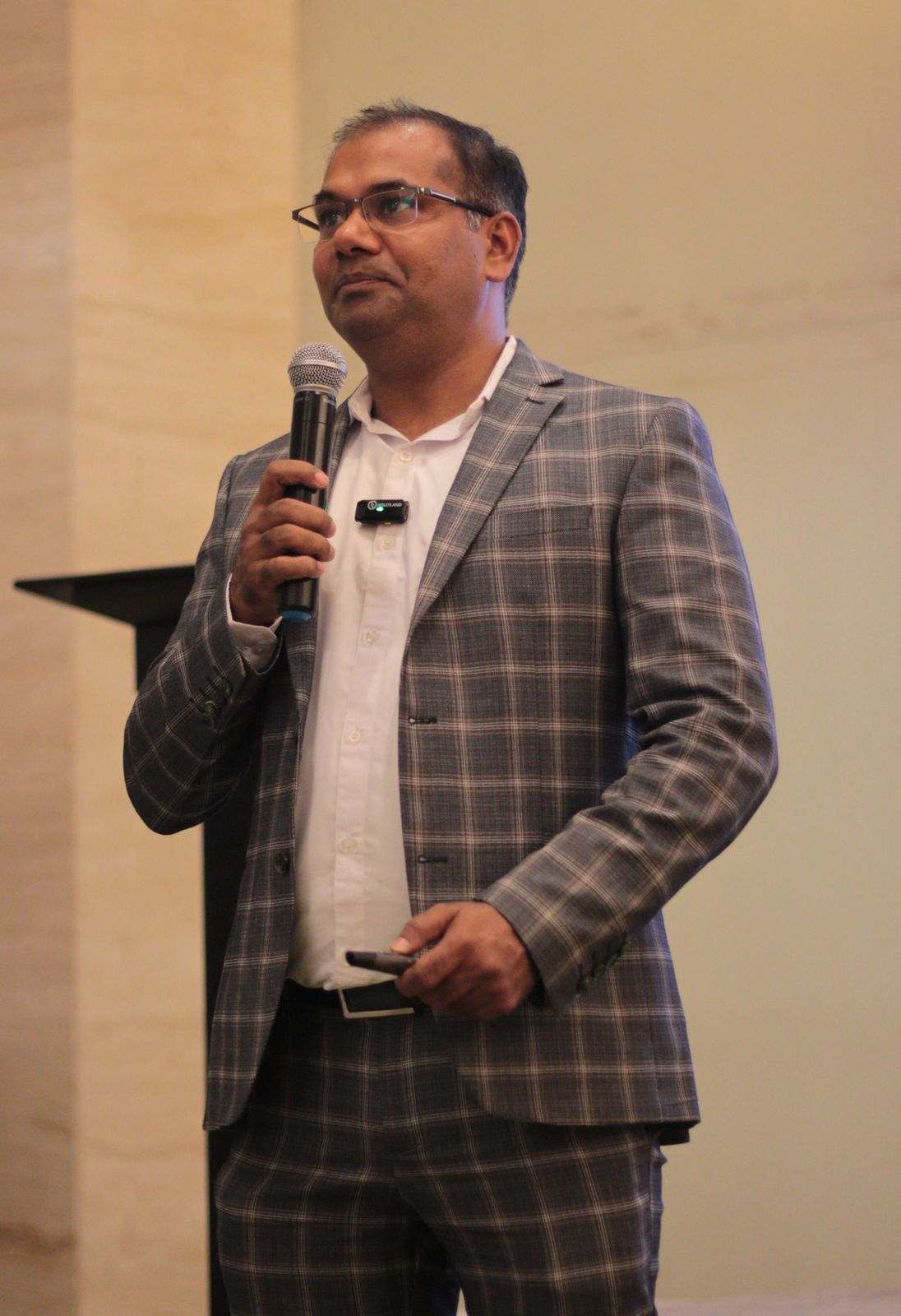 A presenter in a checked suit speaking into a microphone