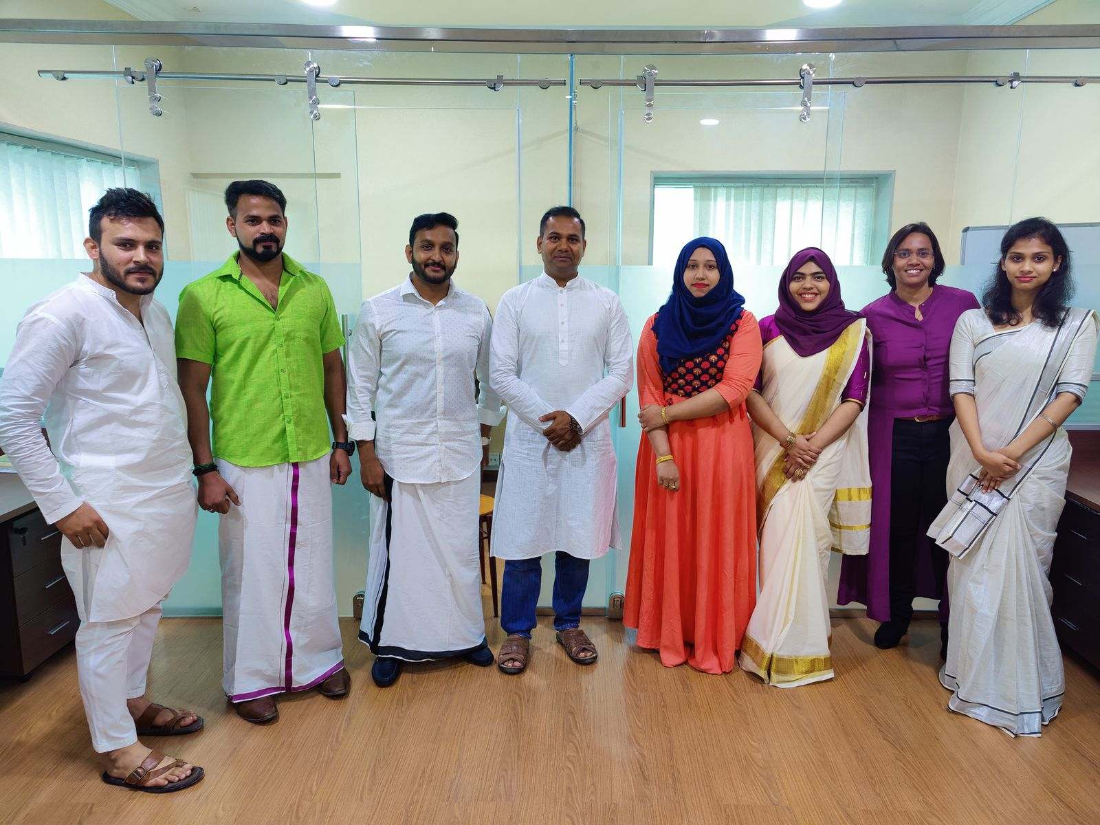 Eight Missan staff in kasavu saris, mundu and kurtas standing in a line in the office